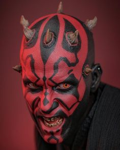 a close up of a person wearing a red and black mask with horns on their head