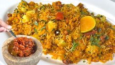 a white plate topped with rice and vegetables next to a bowl filled with oranges