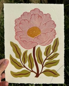 a hand holding up a piece of paper with a flower painted on it's side