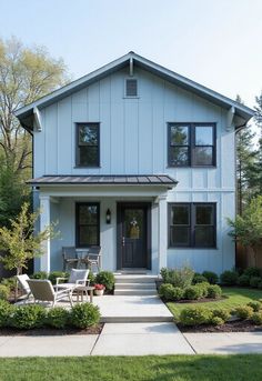 a white house with black windows and two chairs on the front lawn in front of it
