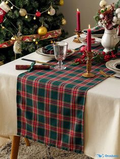 the table is set for christmas dinner in front of the tree with ornaments on it