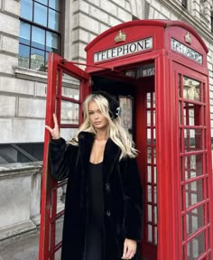 a woman standing in front of a red phone booth with her hand up to the side
