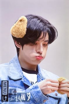 a young man wearing a denim jacket and holding a doughnut in his hand while looking down at the ground