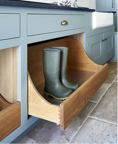 a pair of rubber boots sitting in a wooden cabinet drawer under a counter with blue cabinets