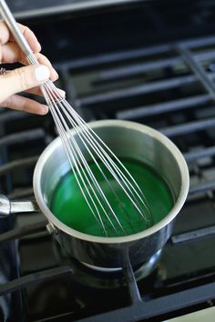 a person whisking green liquid into a saucepan