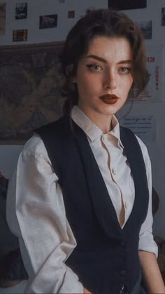 a woman wearing a vest and white shirt is posing for the camera with her hands on her hips