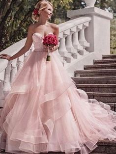a woman in a pink wedding dress is standing on some stairs with her bouquet and looking at the camera