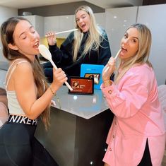 two women are brushing their teeth while another woman looks at the mirror behind them and holds a toothbrush in her mouth