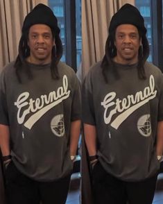 two men in matching t - shirts and beanies standing next to each other near a window