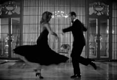 a man and woman dancing in an old fashion dance studio with glass doors behind them