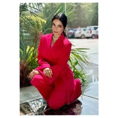 a woman in a red suit is sitting on a shiny surface and posing for the camera