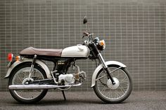 a white and black motorcycle parked in front of a brick wall with a bird on it's seat