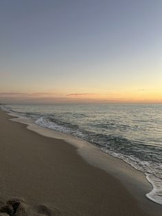 the sun is setting over the ocean with waves coming in to shore and footprints on the sand