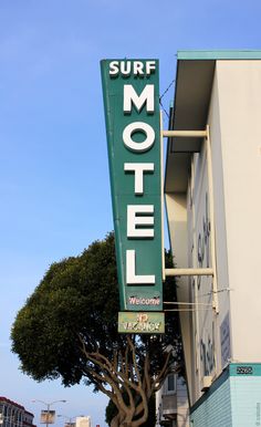 the surf motel sign is green and white with trees in front of it on a sunny day