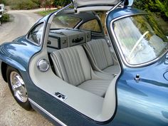 the interior of an old blue car with its doors open and seats down, parked on a gravel road