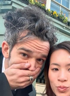 a man covering his face next to a woman with her hand on her cheek,