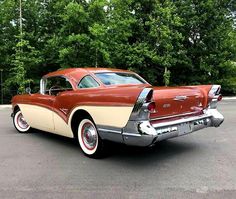 an old red and white car parked in a parking lot next to some green trees