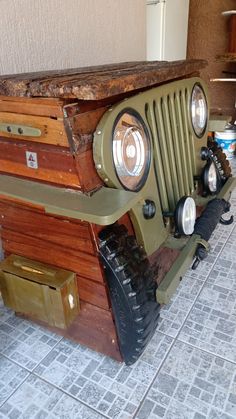 an old green jeep is sitting on the floor in front of a wall and some other items