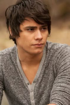 a close up of a person wearing a cardigan and holding a cell phone in his hand