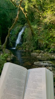 an open book sitting on top of a wooden table next to a river and forest