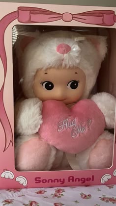 a pink and white teddy bear holding a heart in a pink box with the word hug me written on it