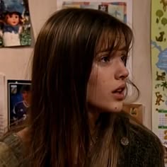 a woman with long brown hair standing in front of a wall full of pictures and posters
