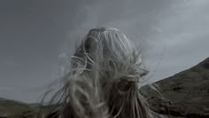 the back of a woman's head with long white hair and mountains in the background