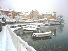 snow is falling on the ground and boats are sitting in the water near some buildings