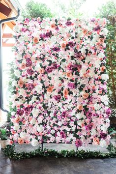 an artificial flower wall is shown in front of a large window with pink and white flowers on it