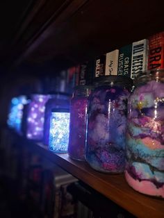 jars filled with different colored liquid sitting on top of a wooden shelf next to books