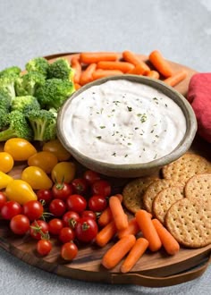 a plate full of veggies and dip with crackers, tomatoes, broccoli
