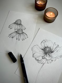 two drawings of flowers on paper next to a candle