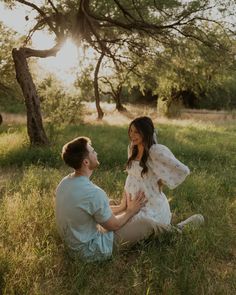 a man kneeling down next to a woman in a field with trees and grass behind them