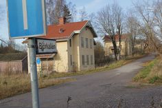 an old run down building with a blue street sign next to it and trees in the background