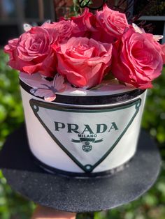 pink roses are in a white bucket with the prada logo on it, sitting on top of a black table