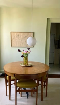 a dining room table with flowers in a vase on it and two chairs at the end