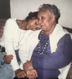 an older woman sitting on top of a couch next to a younger woman with her arm around her shoulder