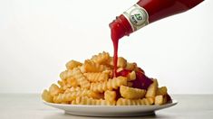 a person pouring ketchup on some french fries