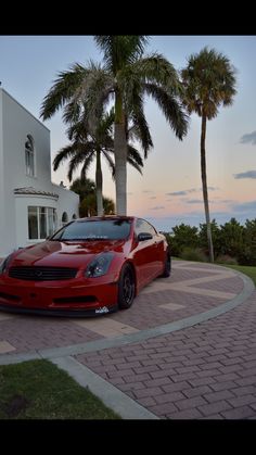a red sports car parked in front of a white house with palm trees around it