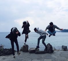 four people jumping in the air with their skateboards over some rocks by the water