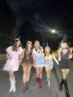 four women dressed in costumes are walking down the street at night with one woman taking a selfie