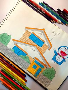 colored pencils are next to a drawing of a house with a cartoon character on it