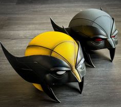 two yellow and black batman masks sitting on top of a wooden floor next to each other