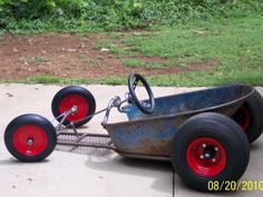 an old metal cart with red wheels on the sidewalk in front of some grass and bushes