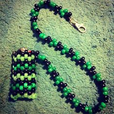 a green and black beaded necklace laying on top of a carpeted floor next to a keychain