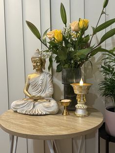 a buddha statue sitting on top of a table next to a vase filled with flowers