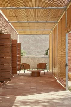 an outdoor covered patio area with two chairs and a coffee table on the ground under a pergolated roof