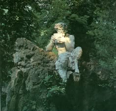 a statue of a man sitting on top of a rock next to trees and bushes