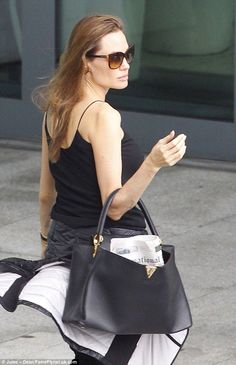 a woman walking down the street carrying a black purse
