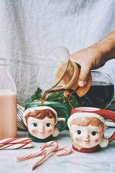 a person pouring milk into two mugs with candy canes